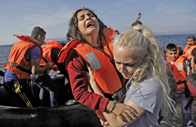 2015eko urrian egina da Catholic News Service hedabideak eskainitako argazki hau: Greziako Lesbos uhartera txalupa pneumatikoz beste iheslariekin batera iritsi den neskato siriarrari lehorreratzen laguntzen dio boluntario batek. Kanpaleku sorta batean ari