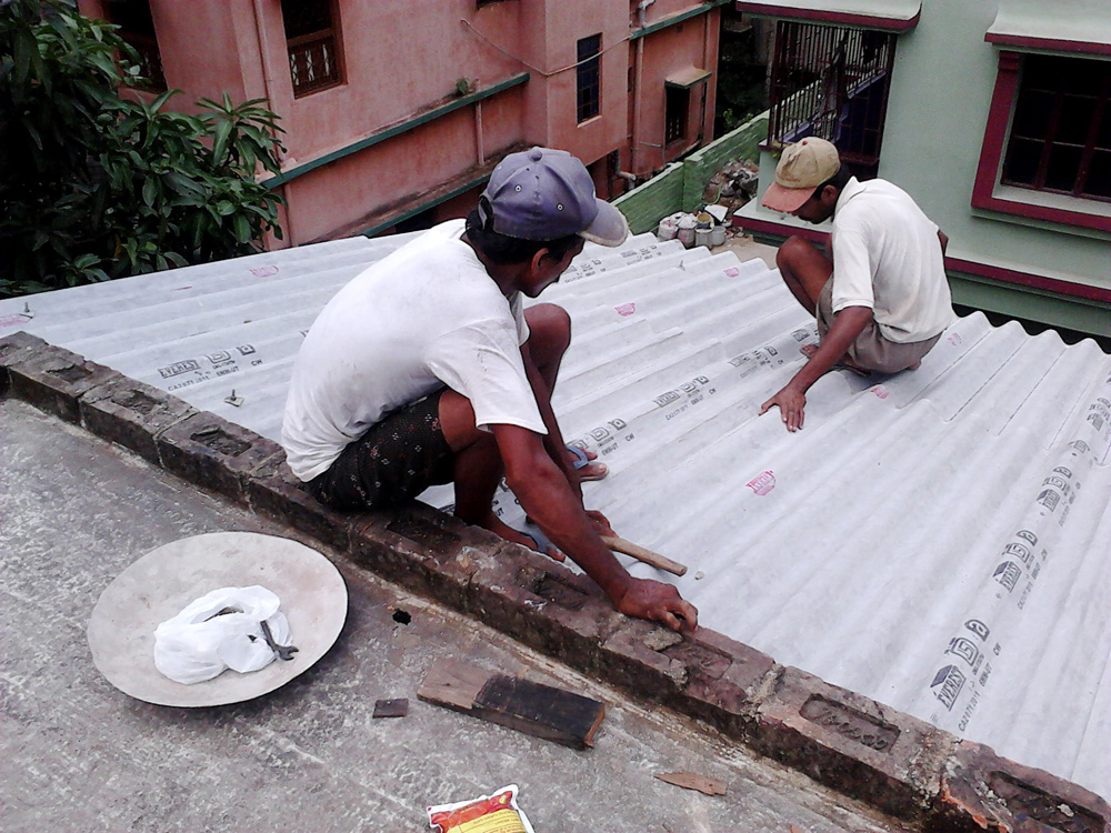 Indian amiantoz egindako teilatua jartzen 2011n. Everest Asbestos Cement irakur daiteke teilen itsasgarrietan, egun abestoarekin lan egiten duen enpresa ugarietako bat. (Arg.: Wikimedia Commons)